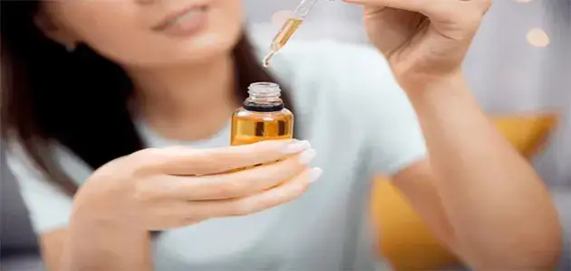 قطرات زيت الجوجوبا تنساب من قطّارة على اليد لتوضيح قوام زيت الجوجوبا النقي